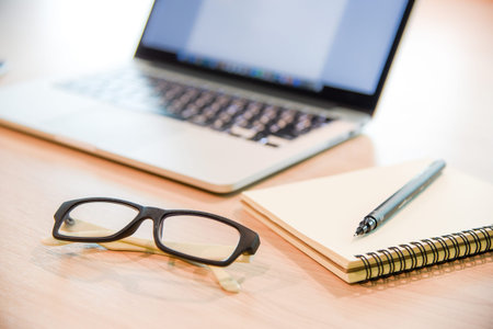 Glasses, binder notebook, pen and laptop on wooden office desk, use for background in business management and learn education conceptsの写真素材