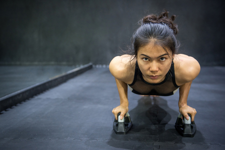 Young Asian athlete woman doing push up with push-up bars on the floor, sport and training in fitness gym conceptsの写真素材