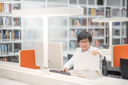 Young Asian university student working with laptop computer and notebook in library, self learning and college lifestyle conceptsの写真素材