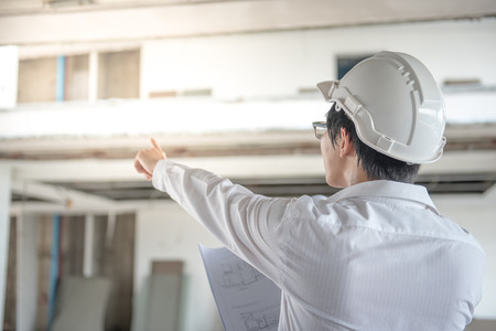 Engineer or Architect checking architectural drawing while wearing a personal protective equipment safety helmet at construction site. Engineering, Architecture and building construction conceptsの写真素材