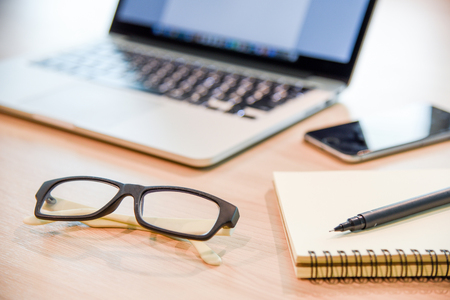 Glasses, binder notebook, pen and laptop on wooden office desk, use for background in business management and learn education conceptsの写真素材
