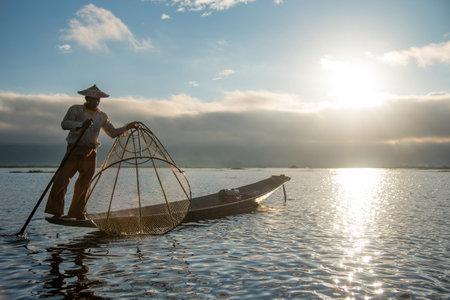 NYAUNGSHWE, MYANMAR - DECEMBER 18, 2016 : Burmese Intha fisherman with traditional fishing net on the boat in Inle lake at sunrise.のeditorial素材