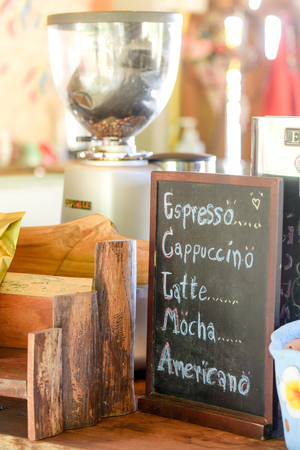 list of coffee menu on chalkboard (espresso, cappuccino, latte, mocha, americano) in coffee shop, handmade cafe decoration on counter topの写真素材