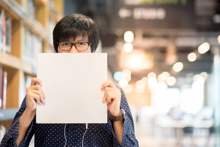 Young Asian man student with eyeglasses lifting white book in library, education research and self learning in university life conceptsの写真素材