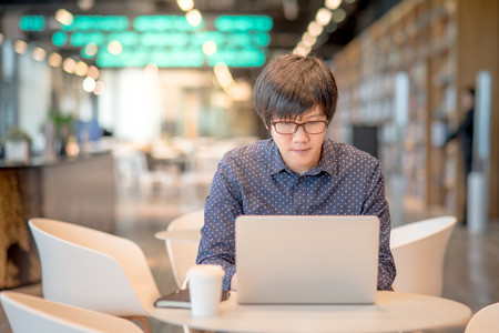 Young Asian businessman working with laptop computer in coffee shop. entrepreneur and freelance lifestyle conceptsの写真素材