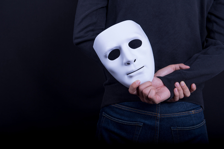 Mystery man holding white mask in the back. Anonymous social masking concept.の写真素材