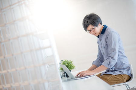 Young Asian man dressed in casual style working in cafe with his laptop computer. Digital nomad and IT modern lifestyle, Co working space for freelance jobsの写真素材