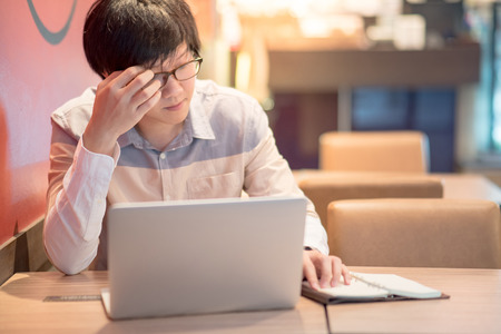 Young Asian business man feeling stressed, tired and headache during working with laptop computer in cafe. freelance lifestyle in workspace.の写真素材