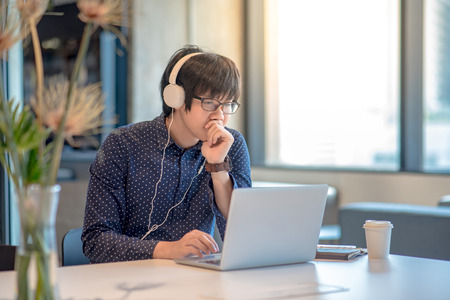 Young Asian businessman dressed in casual style thinking and working with his laptop computer in office workspace. urban lifestyle and modern technology conceptsの写真素材