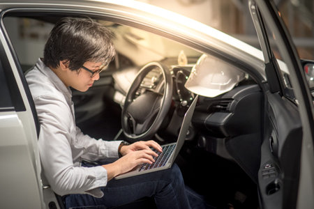Young Asian Engineer or Architect working with laptop computer while sitting in his car. Mechanical...