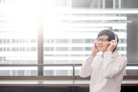 Young Asian man with headphones listening to music in public building. modern IT lifestyle concept.の写真素材