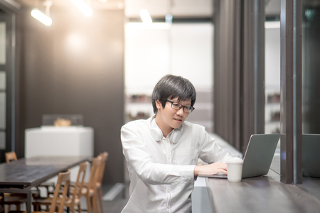 Young Asian man dressed in casual style working in cafe with his laptop computer. Digital nomad and IT modern lifestyle, Co working space for freelance jobsの写真素材