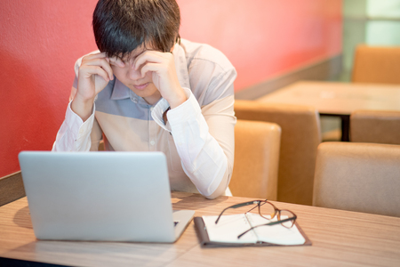 Young Asian business man feeling stressed, tired and headache during working with laptop computer in cafe. freelance lifestyle in workspace.の写真素材
