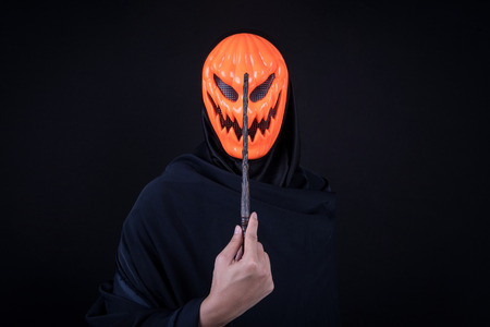 Mystery man with orange pumpkin evil mask holding magic wand on black background, Halloween night costume conceptの写真素材