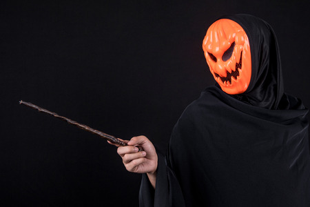 Mystery man with orange pumpkin evil mask holding magic wand on black background, Halloween night costume conceptの写真素材