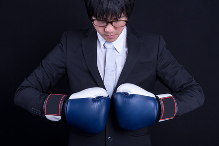 young asian business man wearing suit and posing  with blue boxing gloves in black background studio. business man fight pose conceptの写真素材