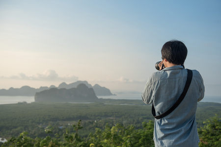 Young Asian man taking photo of beautiful scenery, male travel photographer and summer landscape in Thailand.の写真素材