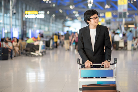 Young asian man with his luggage on airport trolley waiting for check in at airline counter in the international airport terminal, business travel conceptの写真素材