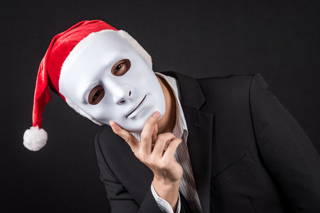 Young Asian businessman wearing white mask and santa hat, male anonymous worker wearing party costumes on black background. Christmas and New Year holiday conceptsの写真素材