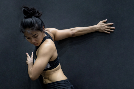 young asian woman wearing sportswear stretching her arm on black wall in fitness gym, exercise for healthy lifestyle conceptの写真素材