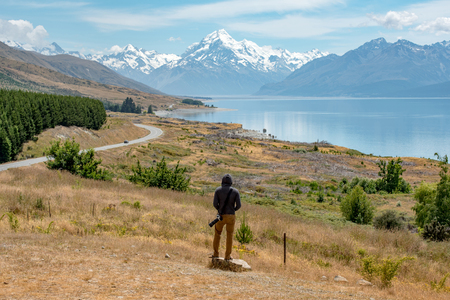 Young male photographer in hoody watching at Mount Cook, one of the most famous snowy mountain at peterâs lookout in South Island, New Zealand. Travel in summer conceptの写真素材