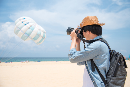 Young Asian man photographer in jean shirt take photo of parasailing on the beach of Phuket, Thailandの写真素材