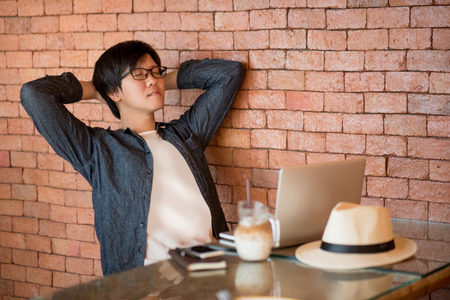 Young Asian man in relax posing while working with laptop computer in cafe. Digital nomad or freelance lifestyle conceptsの写真素材