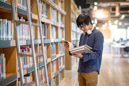 Young Asian man university student reading book in library, education research and self learning in university life conceptsの写真素材