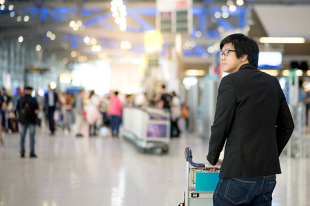 Young asian man with his luggage on airport trolley waiting for check in at airline counter in the international airport terminal, business travel conceptの写真素材