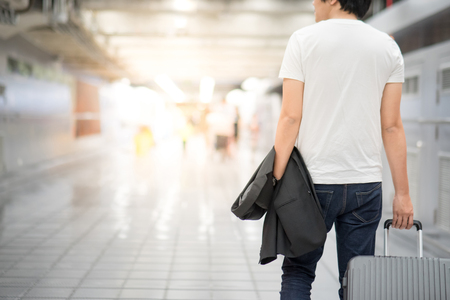 Young Asian casual man holding suit and luggage while walking in airport terminalの写真素材