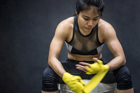 Asian female boxer wearing yellow strap on wrist. Beautiful young woman with muscular body preparing for boxingの写真素材