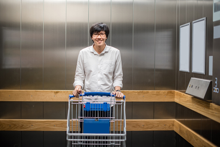 Young Asian man standing with empty trolley cart in lift or elevaror. shopping in warehouse conceptの写真素材