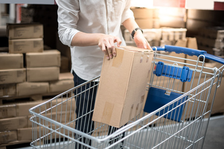 Young man putting paper box into trolley cart in warehouse, shopping warehousing conceptの写真素材