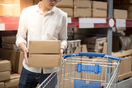 Young Asian man putting paper boxes into trolley cart in warehouse, shopping warehousing conceptの写真素材