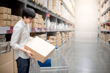 Young Asian man putting paper box into trolley cart in warehouse, shopping warehousing conceptの写真素材