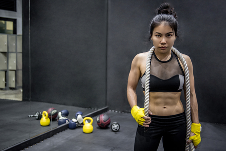 Young Asian gymnast woman posing with gymnastics rope on shoulders and other equipments for exercise or workout in fitness gymの写真素材