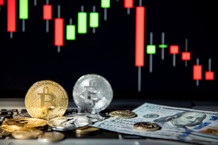 Studio shot of bitcoin gold silver coins and dollar bank note on laptop keyboard with basic candlestick green red graph price in background. Worldwide cryptocurrency and digital payment conceptsの写真素材