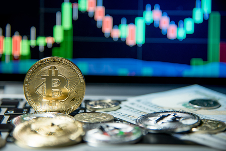 Studio shot of bitcoin gold silver coins and dollar bank note on laptop keyboard with basic candlestick green red graph price in background. Worldwide cryptocurrency and digital payment conceptsの写真素材