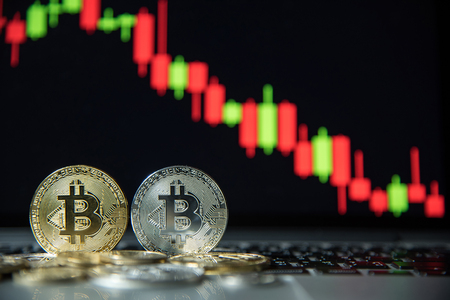 Studio shot of bitcoin gold and silver coins on laptop keyboard with basic candlestick green red graph price in background. Worldwide cryptocurrency and digital payment conceptsの写真素材
