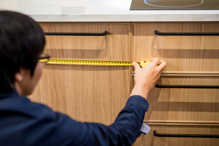 Young Asian man using tape measure for measuring wooden kitchen counter in warehouse. Shopping furniture for home improvement conceptの写真素材
