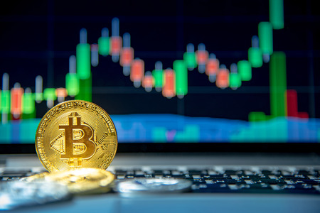 Studio shot of bitcoin gold coin on laptop keyboard with basic candlestick green red graph price in background. Close up and focus on bitcoin. Worldwide cryptocurrency and digital payment conceptsの写真素材