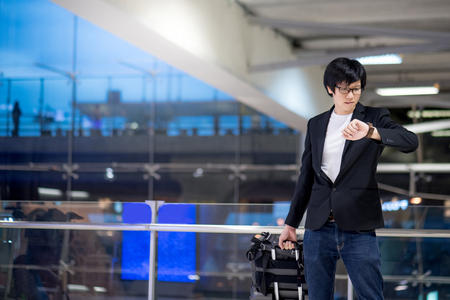 Young asian businessman checking the time from his watch while waiting for check-in in the international airport terminal, business travel conceptの写真素材