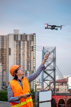 Young Asian engineer flying drone over construction site. Using unmanned aerial vehicle (UAV) for land and building site survey in civil engineering project.の写真素材