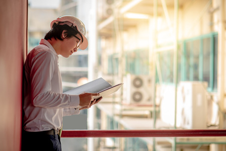 Young Asian Engineer or Architect holding files while wearing personal protective equipment safety helmet at construction site. Engineering, Architecture and construction business conceptsの写真素材