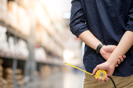 close up of male hand holding yellow tape measure in warehouse. Furniture product design measuring conceptの写真素材