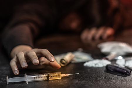 Male junkie hand trying to grab injection syringe of cooked heroine. Hard drug overdose and addiction conceptの写真素材