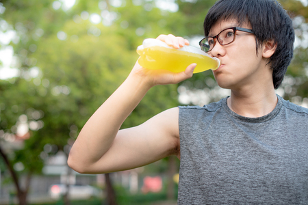 Young Asian man runner with eyeglasses and sport clothes drinking energy drink after jogging in the park. healthy lifestyle with urban running conceptの写真素材