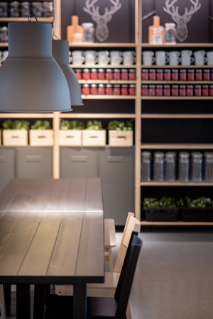 Working wooden table desk with modern lamps overhead and decoration shelves in the background. Coworking space or design office workspace concept.の写真素材