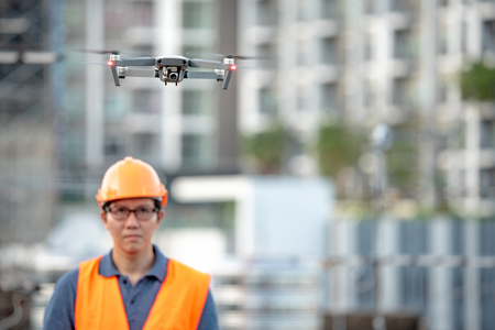 Young Asian engineer flying drone over construction site. Using unmanned aerial vehicle (UAV) for land and building site survey in civil engineering project.の写真素材