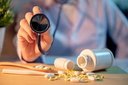 Male Asian doctor holding stethoscope in hospital clinic. Pills spilling out of pill bottles on doctor desk. Medical treatment and health care consultation concepts.の写真素材